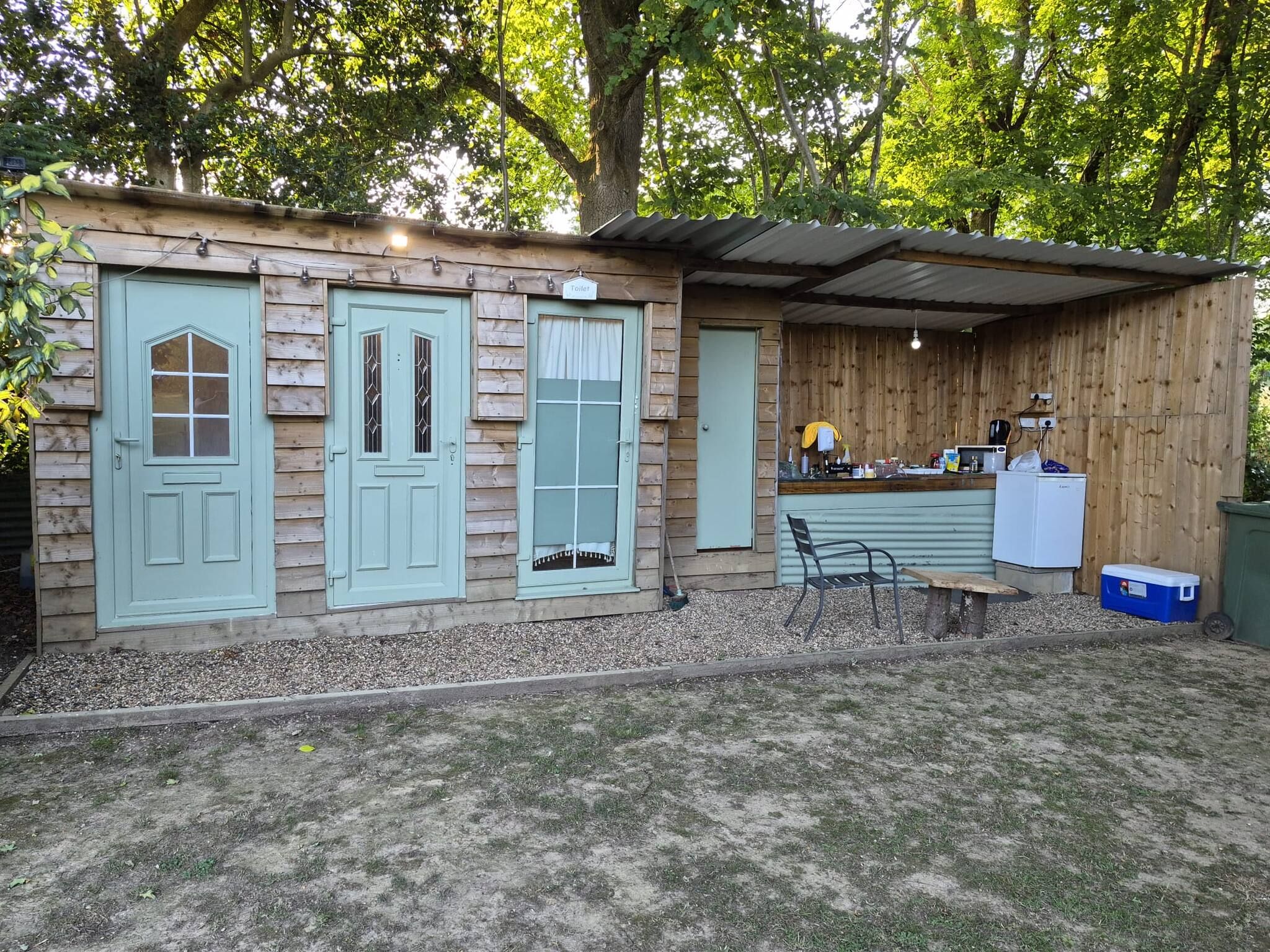 Een houten gebouw in landelijke stijl met drie deuren, een klein terras en een kitchenette.