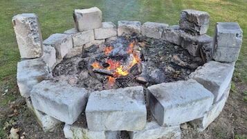 Un hogar de concreto con fuego encendido, rodeado de un césped.