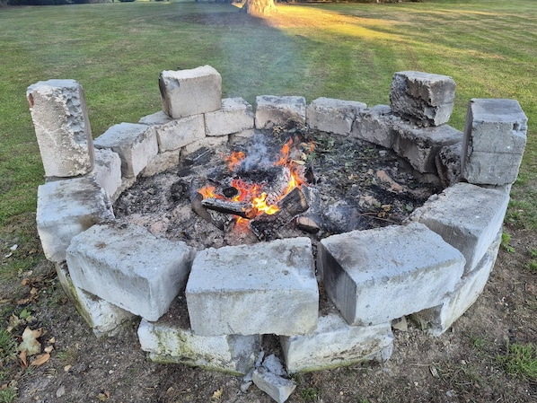 A concrete fire pit with a fire burning inside, surrounded by a grassy area.