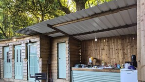 A rustic wooden structure with a kitchen area, a bench, and a trash bin.