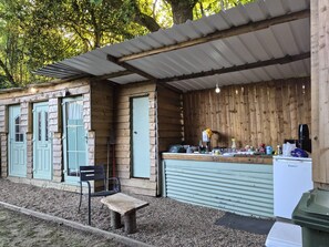 A rustic wooden structure with a kitchen area, a bench, and a trash bin.