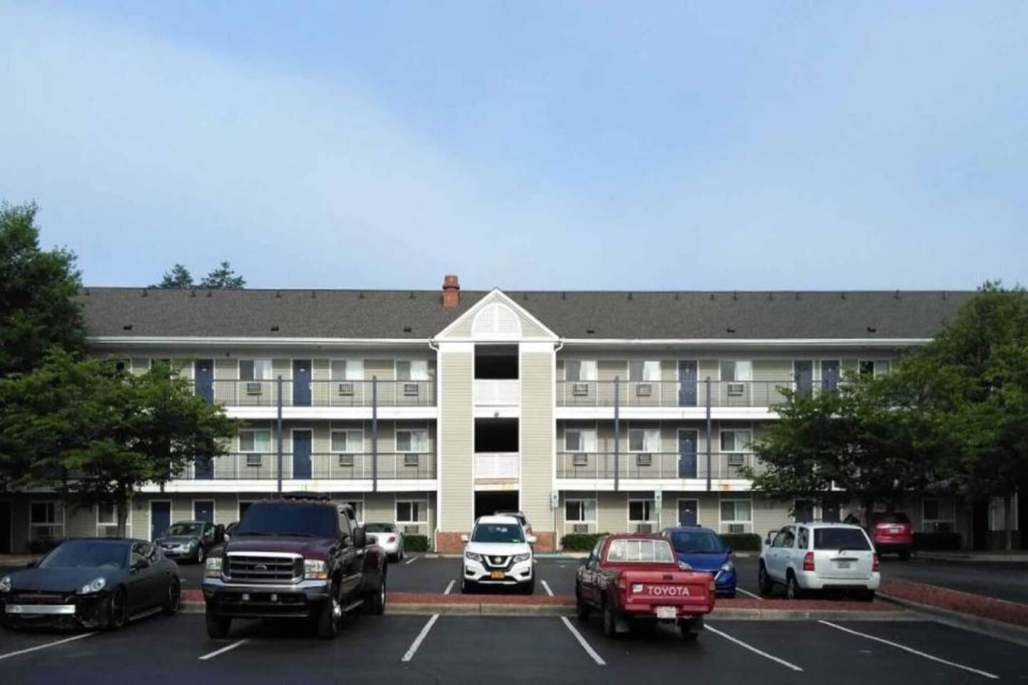 A multi-story building with a central entrance, parking lot, and several parked cars.