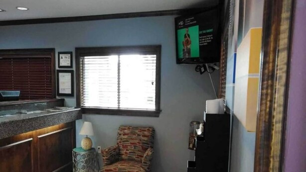 Una habitación con una recepción, una ventana con persianas, un televisor en la pared y una silla estampada.