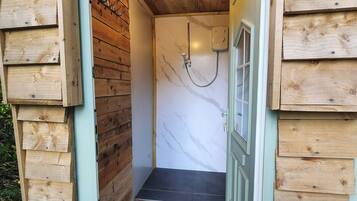 Una cabaña de madera con un baño pequeño que incluye ducha, piso de baldosas y puerta de madera.