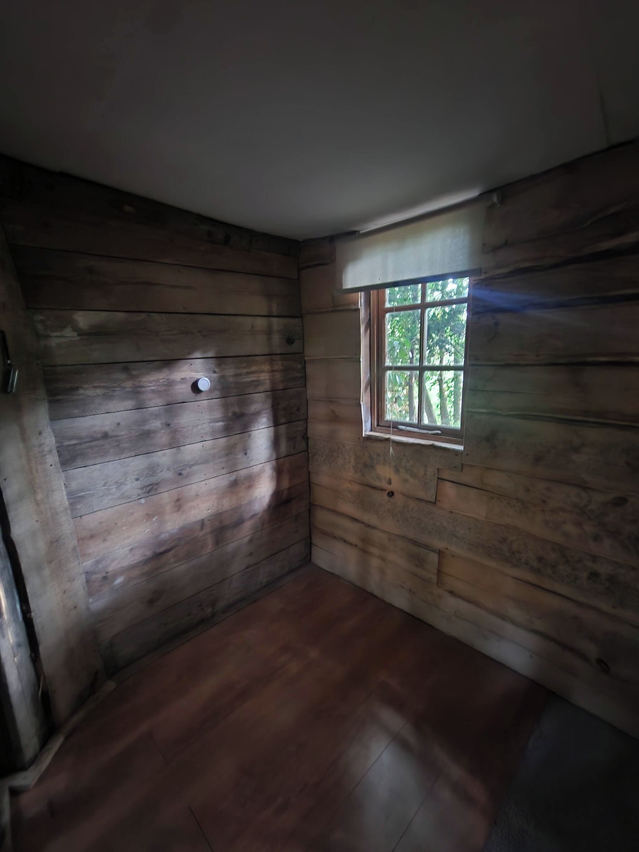 A room with wooden walls and a window with a view of trees.