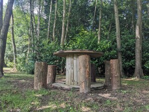 A wooden gazebo in a forested area with a circular base and a flat roof.