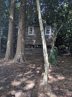 A rustic log cabin surrounded by trees. - Tree House at The Secret Garden (Biddenden)