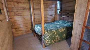 Habitación de cabaña de madera con cama con dosel, piso alfombrado y una ventana.