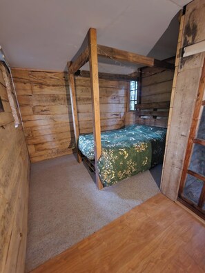 A wooden cabin room with a four-poster bed, carpeted floor, and a window. - Tree House at The Secret Garden (Biddenden)