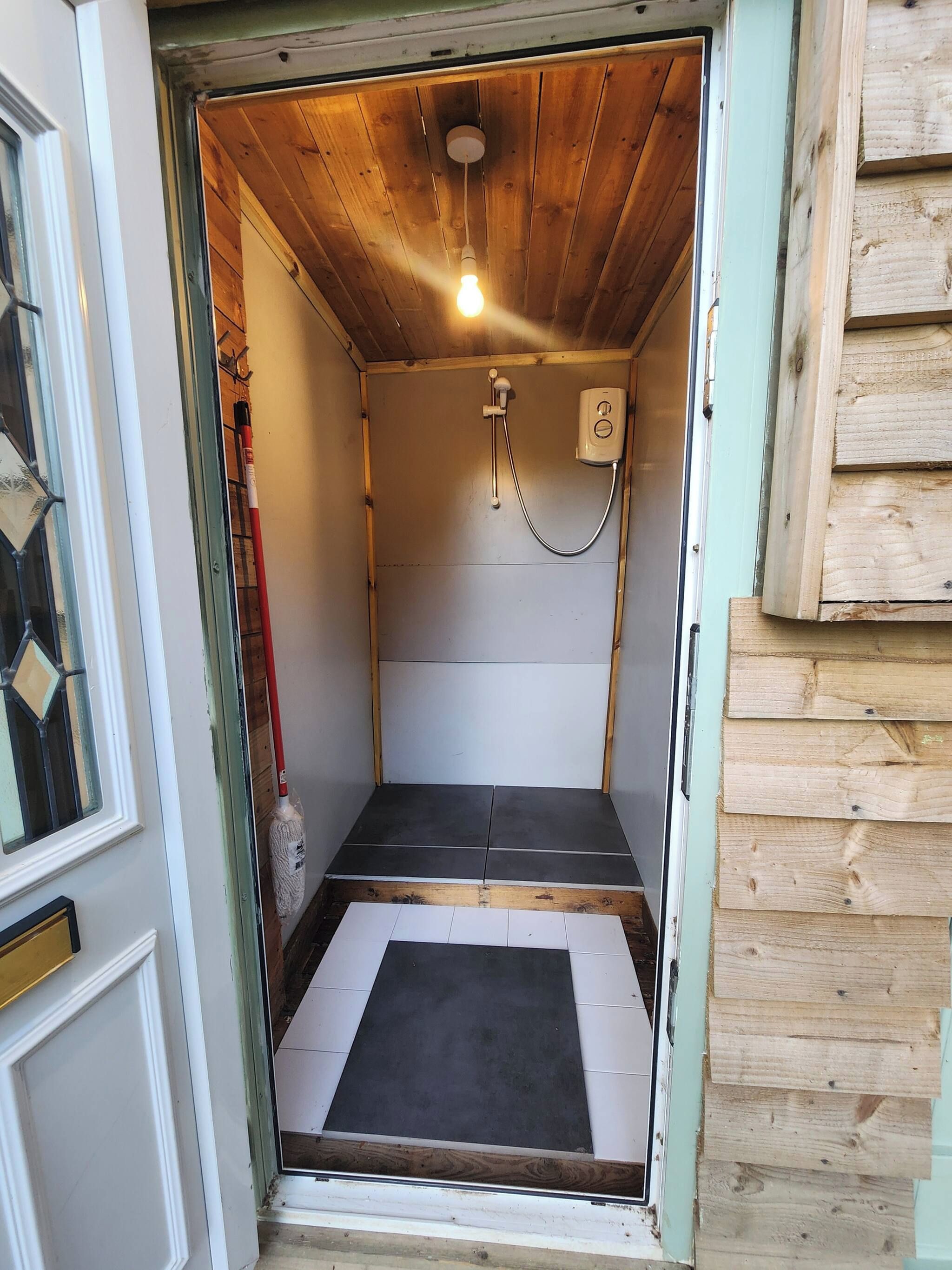 Un petit espace douche fermé, doté d’un plafond en bois, d’un pommeau de douche à main et d’un luminaire.