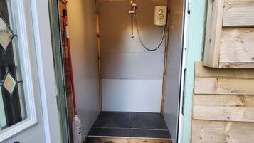 Un petit espace douche fermé, doté d’un plafond en bois, d’un pommeau de douche à main et d’un luminaire.