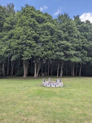 Um campo gramado com uma estrutura de pedra no centro, rodeado por uma floresta densa.