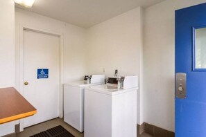 Un lavadero pequeño con lavadora y secadora, una puerta azul y señal de accesibilidad para personas con discapacidad.
