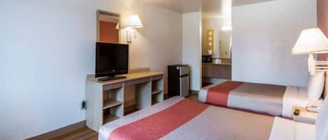 A hotel room with two beds, a television, a desk, and a mirror.
