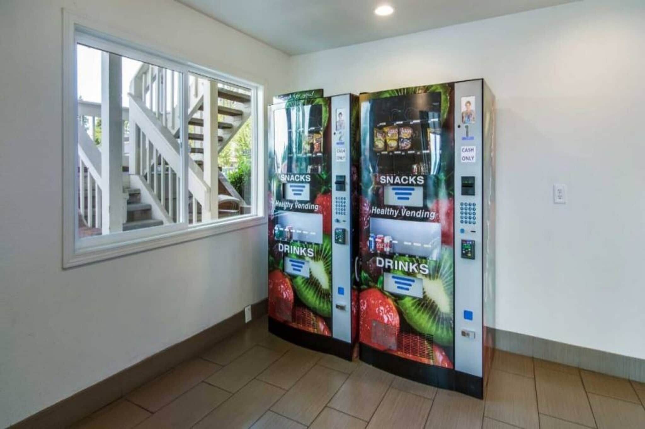 Corredor com duas máquinas de venda automática identificadas como 'Healthy Vending', para lanches e bebidas.