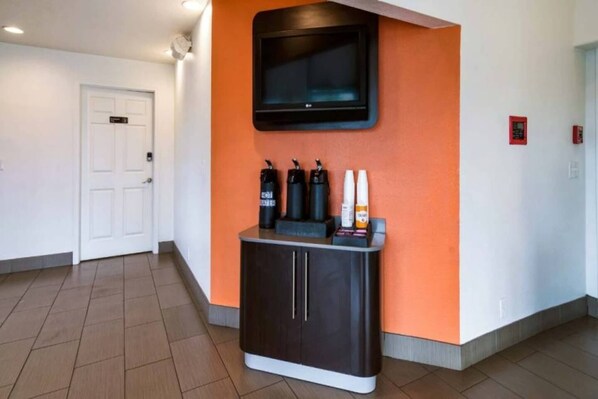 Un pasillo con un armario negro, un televisor montado en una pared naranja y una puerta blanca.