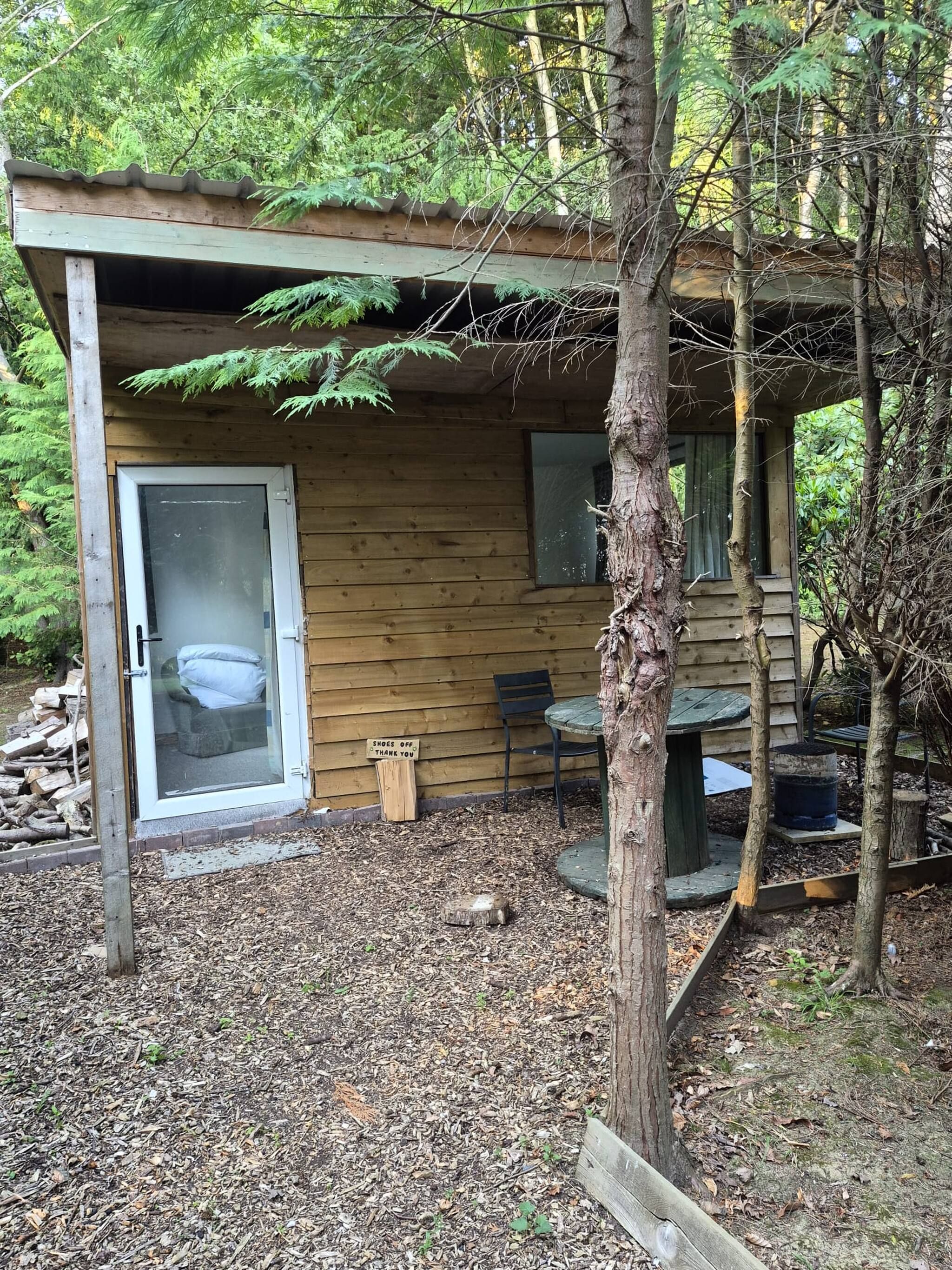 Uma cabana de madeira com porta de vidro, uma mesa e uma cadeira na varanda.