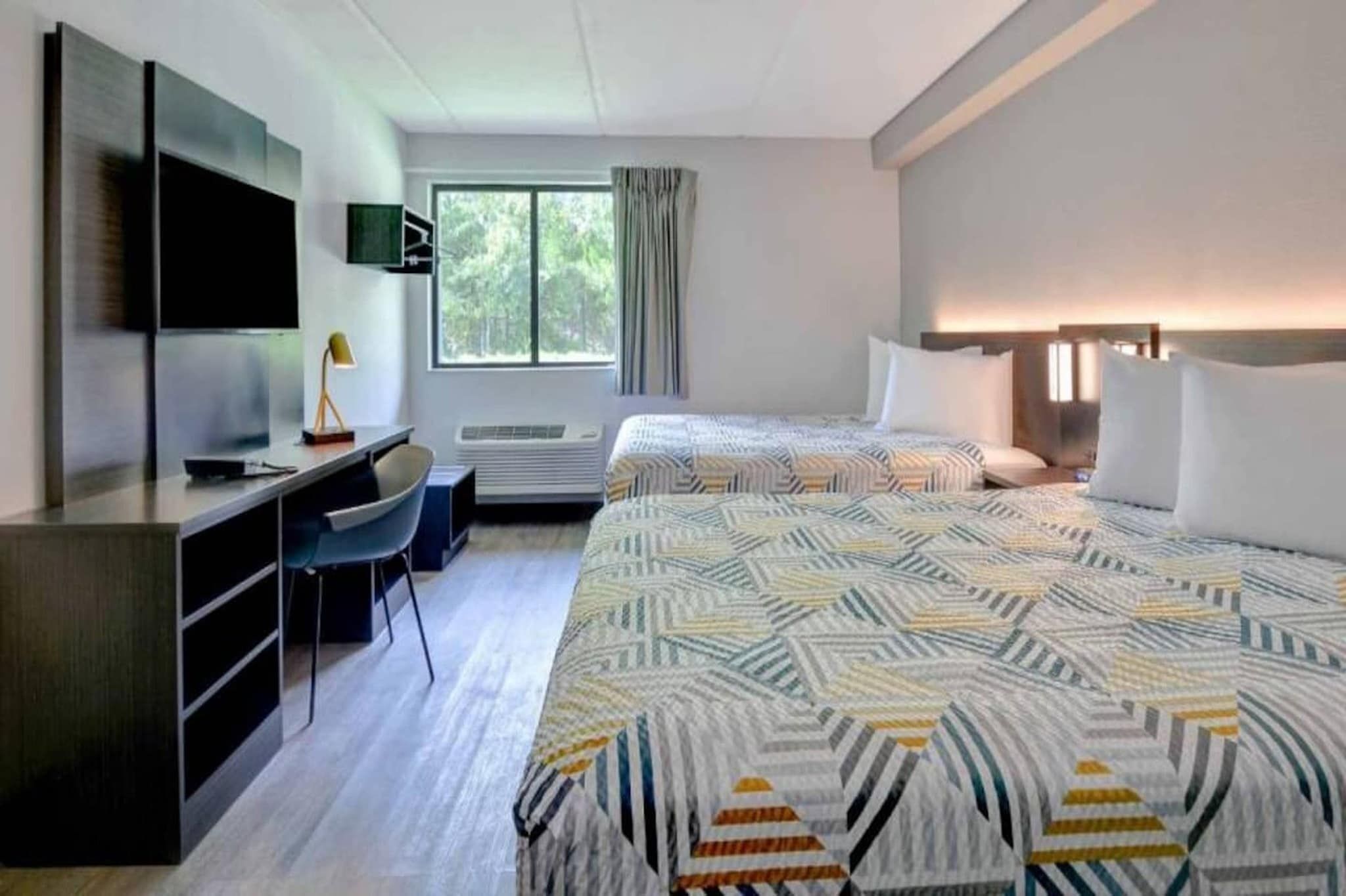 A hotel room with a bed, a desk, a chair, a TV, and a window with curtains.