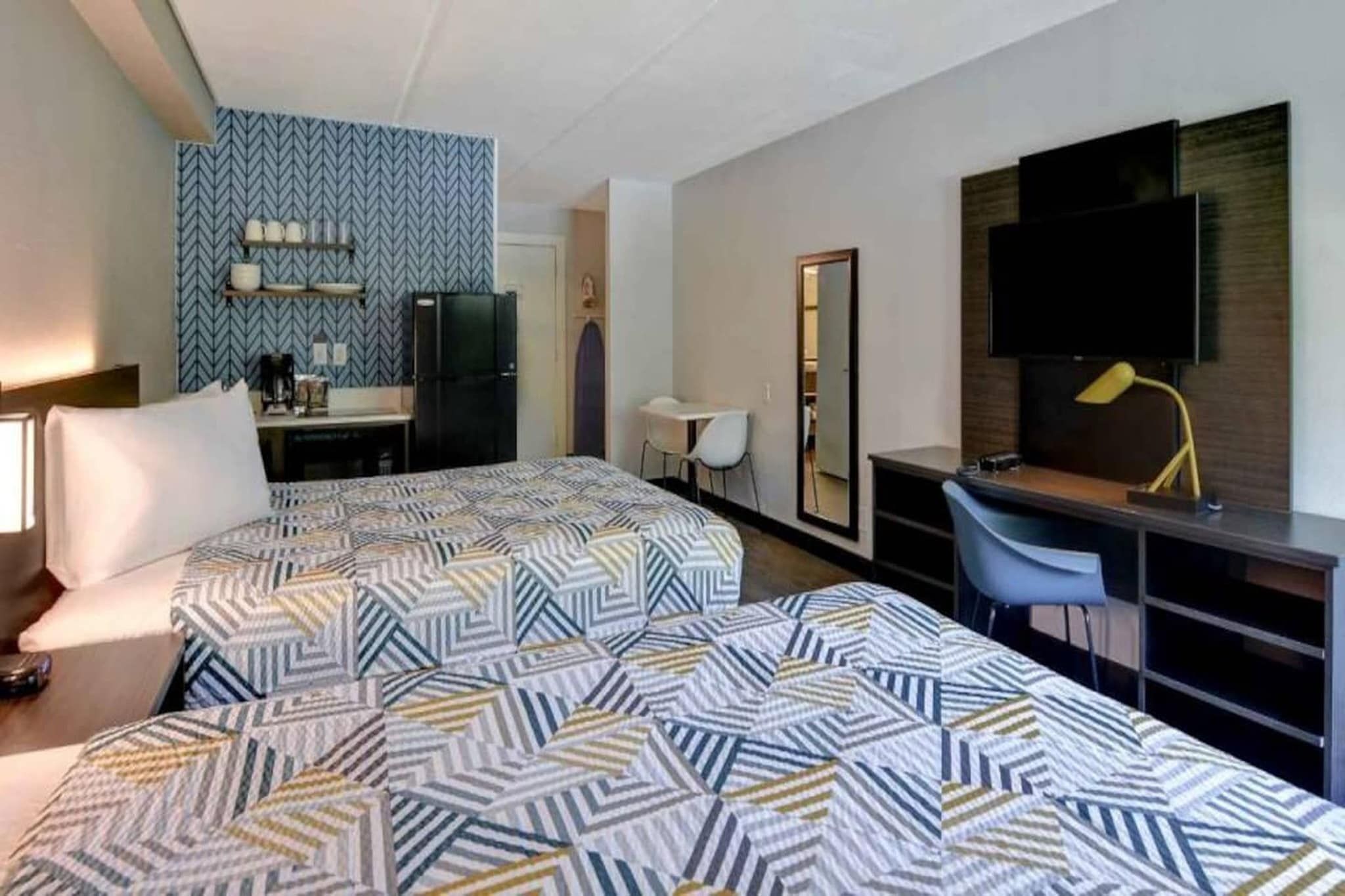 A hotel room with a bed, desk, chair, TV, and a mirror.