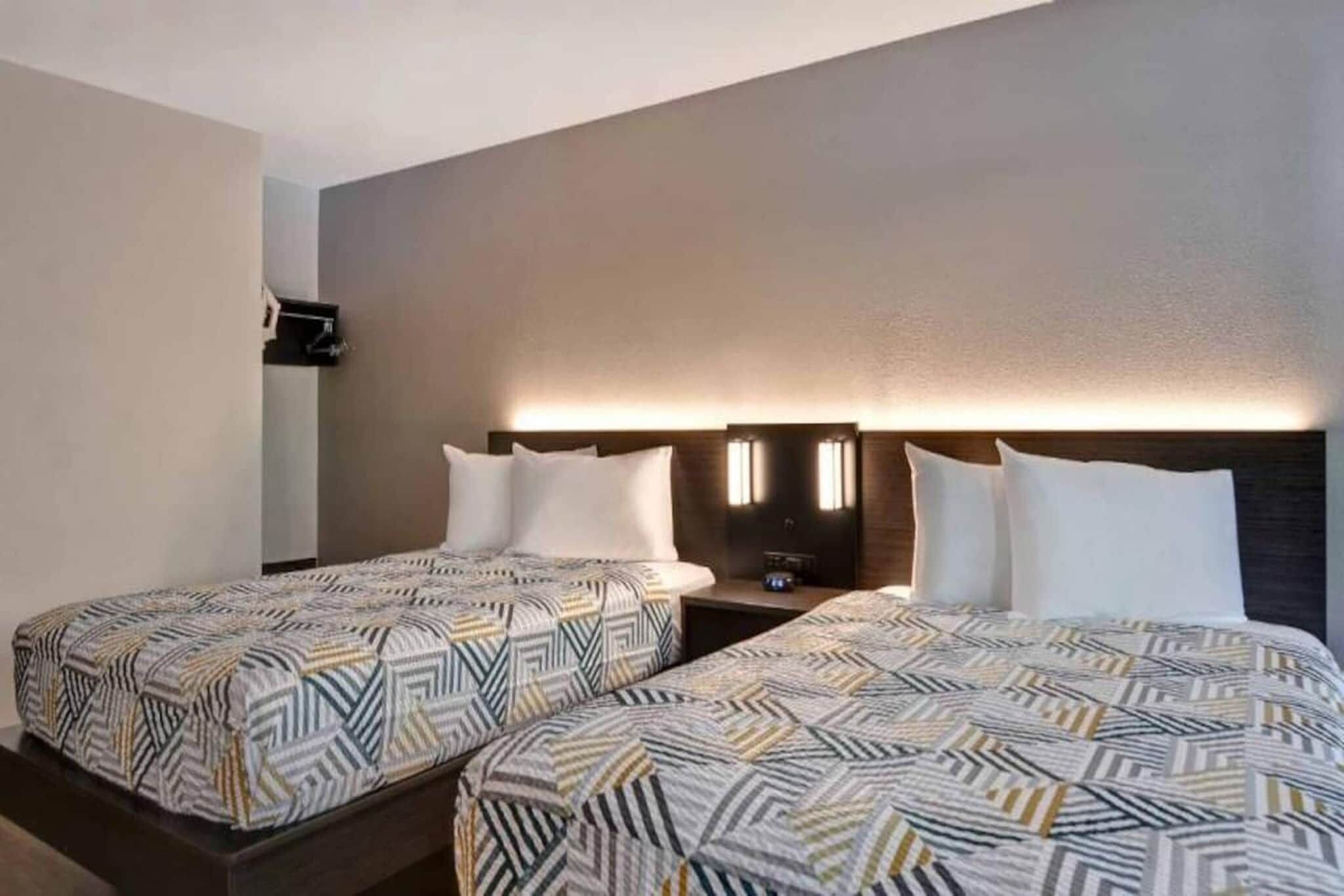 Une chambre d’hôtel avec deux lits, chacun agrémenté de draps à motifs, une table de chevet avec une lampe et un téléviseur fixé au mur.