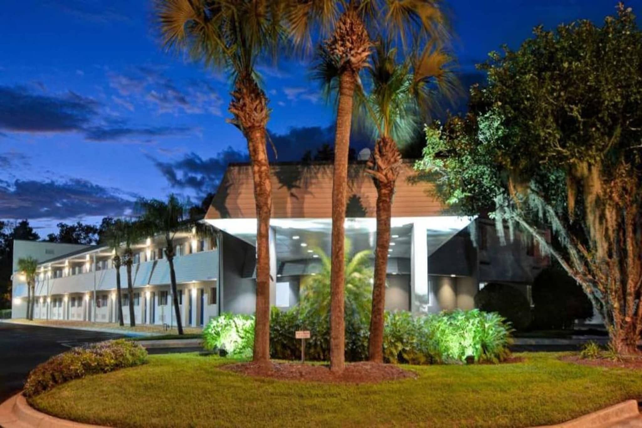 A hotel with a modern design, featuring a large glass facade, palm trees, and a well-maintained lawn.