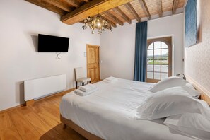Ein Schlafzimmer mit einem Bett, einem an der Wand befestigten Fernseher, einer Holztür und einem Fenster mit Vorhängen.