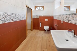 Ein Badezimmer mit Holzboden, einem weißen Waschbecken, einer Toilette und einer Duschkabine.