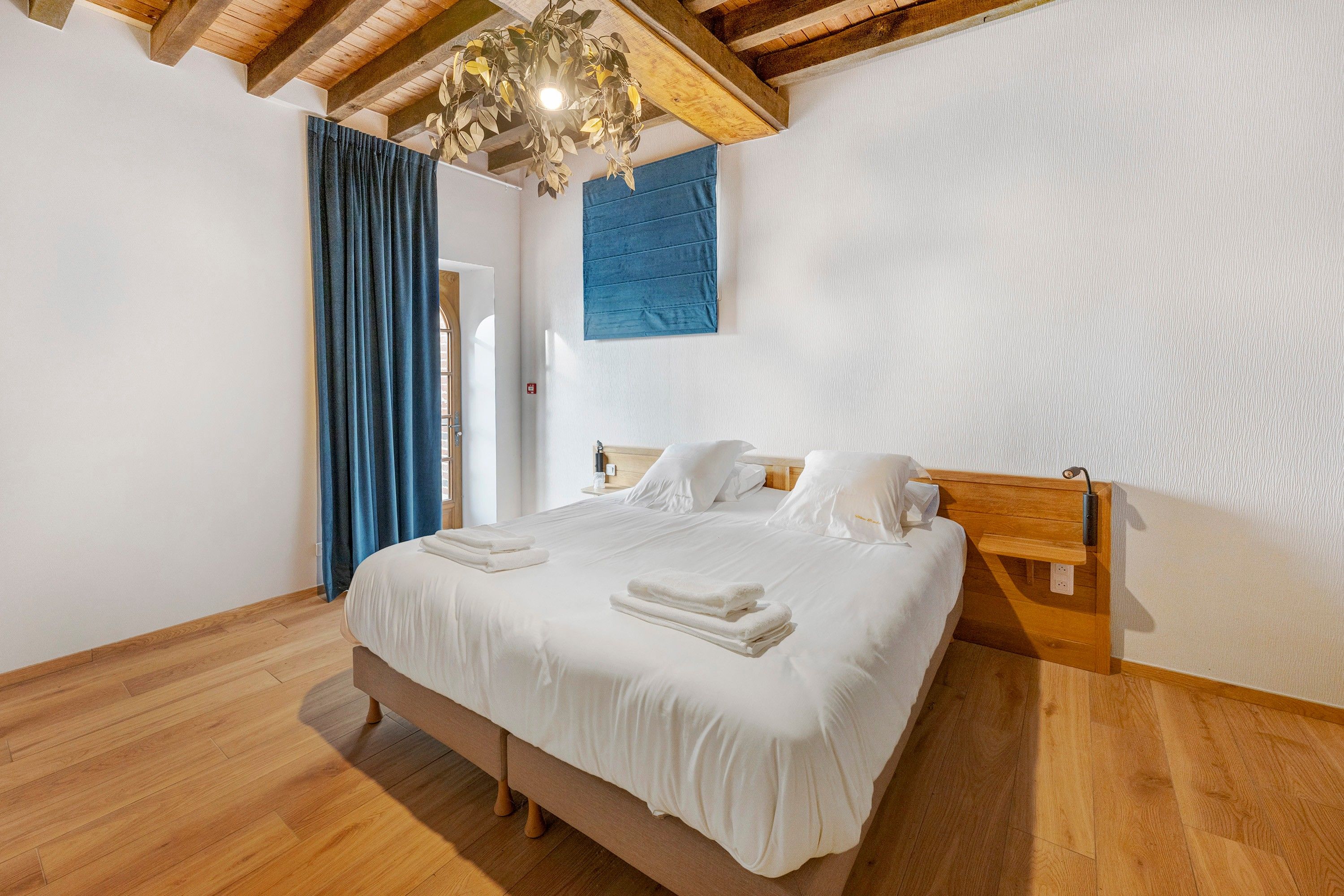 Une chambre à coucher avec un lit en bois, du linge de lit blanc, un rideau bleu et un plafond en bois.