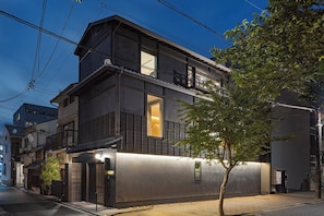 Un bâtiment moderne à deux étages, doté d’un balcon, d’un arbre devant et d’une entrée bien éclairée.