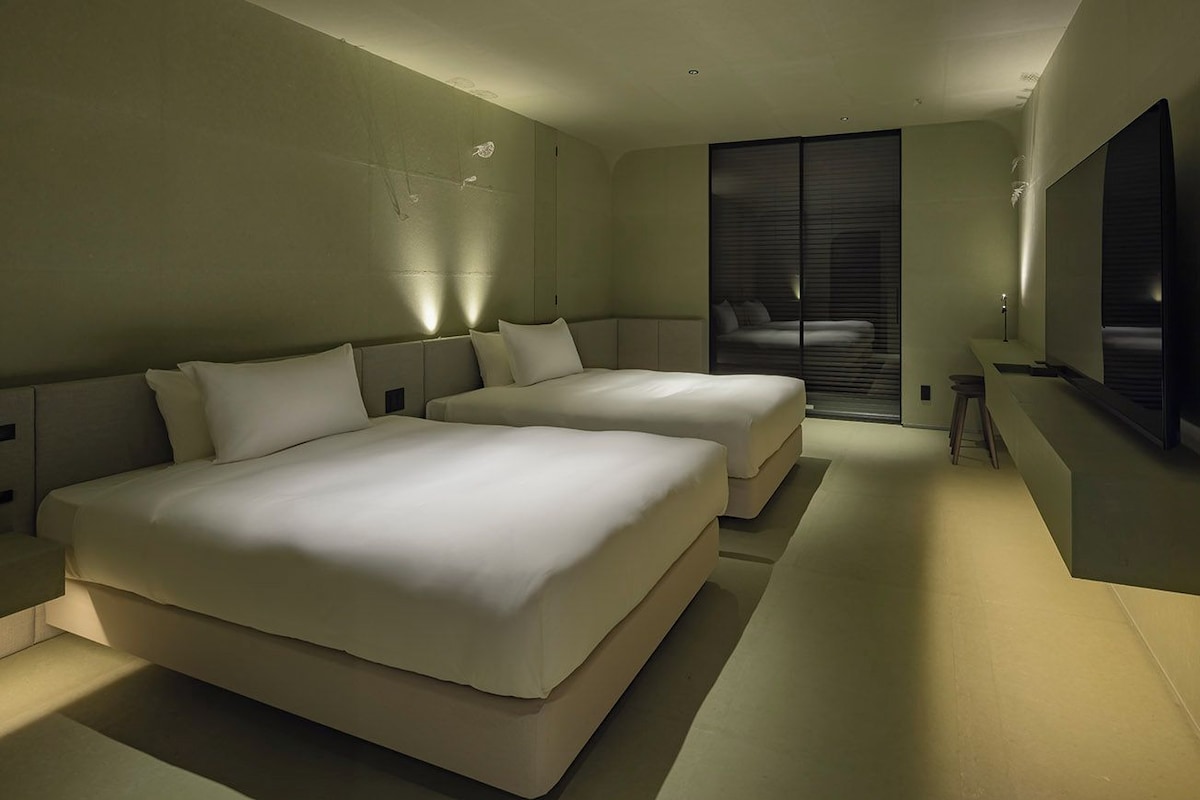 Une chambre d’hôtel moderne avec deux lits, une grande fenêtre et un téléviseur à écran plat.