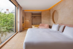 Une chambre d’hôtel moderne dotée d’un grand lit, d’un coin salon et offrant une vue sur l’extérieur grâce à une grande fenêtre.