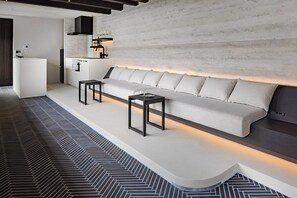 Un espace de vie moderne comprenant un canapé, deux tables d’appoint, un coin cuisine et un sol à motifs.