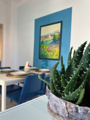 Ein Kaktus im Topf auf einem Tisch mit einem blauen Stuhl und einem Gemälde an der Wand.