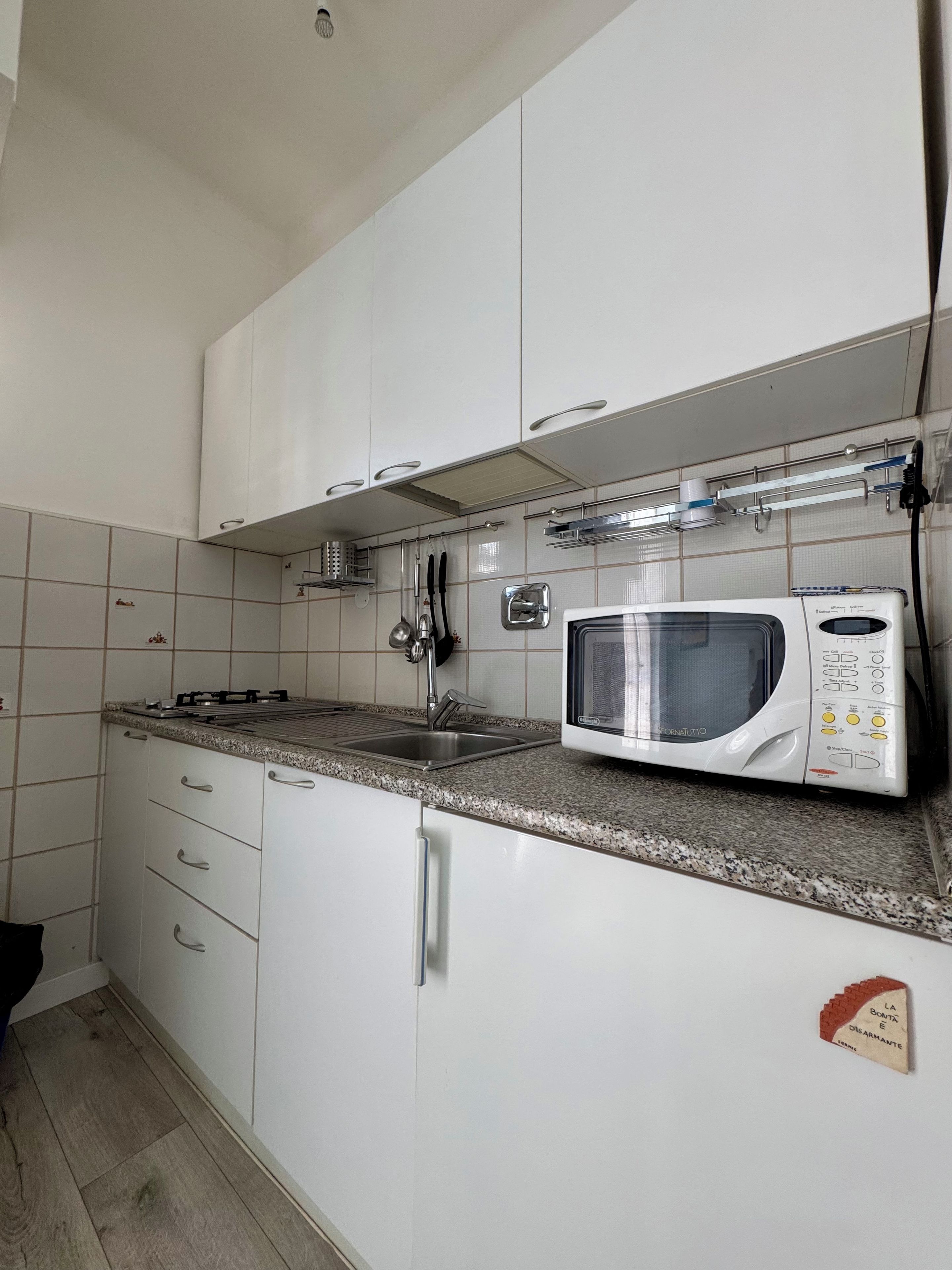 Keittiössä on valkoiset kaapit, graniittitaso, sisäänrakennettu mikroaaltouuni ja ruostumattomasta teräksestä valmistettu pesuallas.