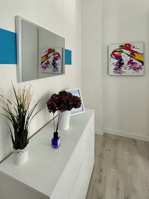 Ein moderner Empfangsbereich mit einer weißen Theke, einem großen Spiegel und zwei gerahmten Kunstwerken an der Wand.