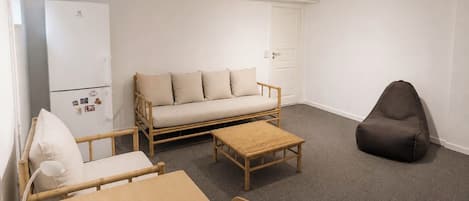 A room with a sofa, a chair, a table, a lamp, a small stool, and a dark bean bag.