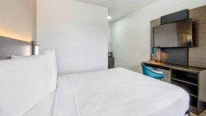 A hotel room with a bed, a desk, a chair, a television, and a small table. - Cozy 1 Queen Bed | Mini Fridge (Austin TX)