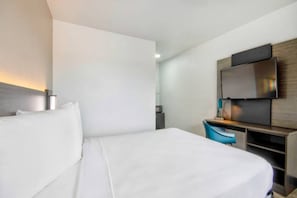 Una habitación de hotel con una cama, un escritorio, una silla, un televisor y una mesita.