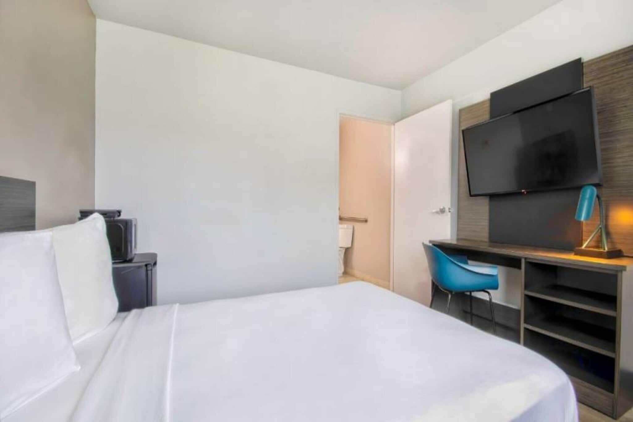 Ein Hotelzimmer mit einem Bett, einem Schreibtisch mit Stuhl, einem Fernseher und einem Kleiderschrank.