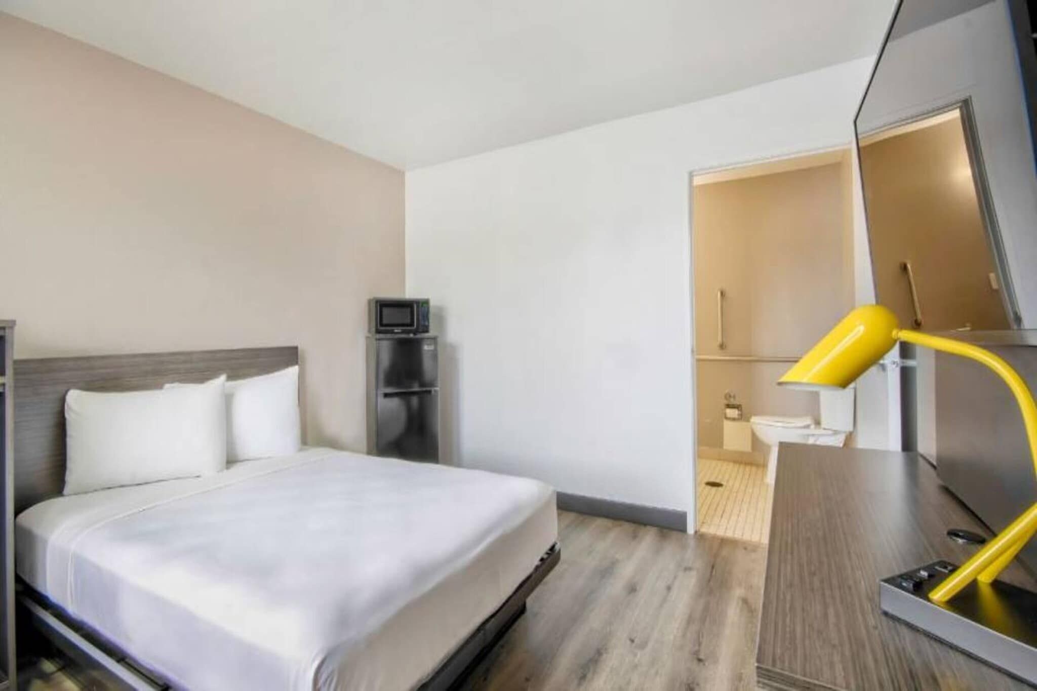 Habitación de hotel con cama, escritorio, silla, televisor y baño visible a través de una puerta abierta.