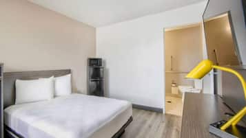 Habitación de hotel con cama, escritorio, silla, televisor y baño visible a través de una puerta abierta.