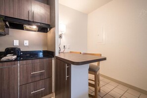 A compact kitchen with dark wood cabinets, a black countertop, and a small dining area with a chair. - 2 Queen bed | Smoking (Duluth)