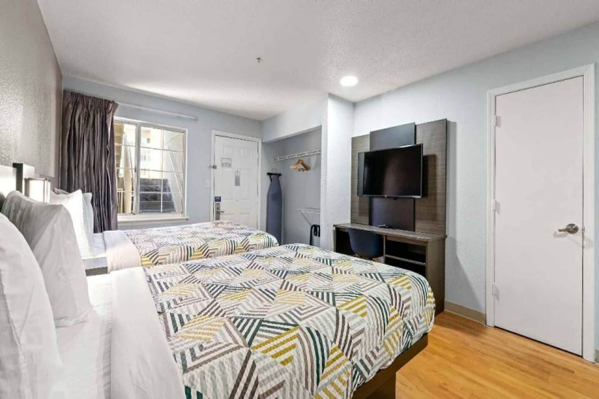 Habitación de hotel con dos camas, un televisor y una ventana con cortinas.