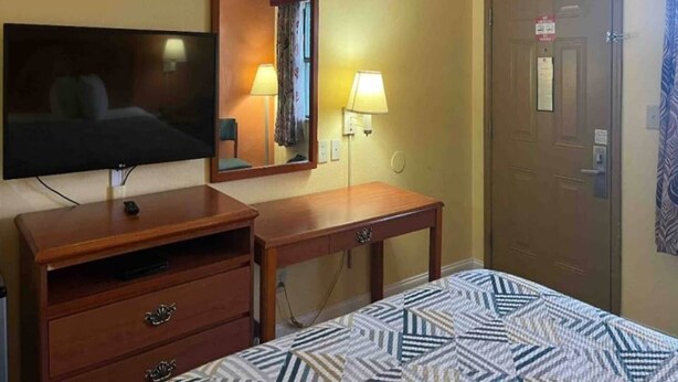 Una camera d'albergo con un letto, una televisione, una scrivania, uno specchio e una porta.
