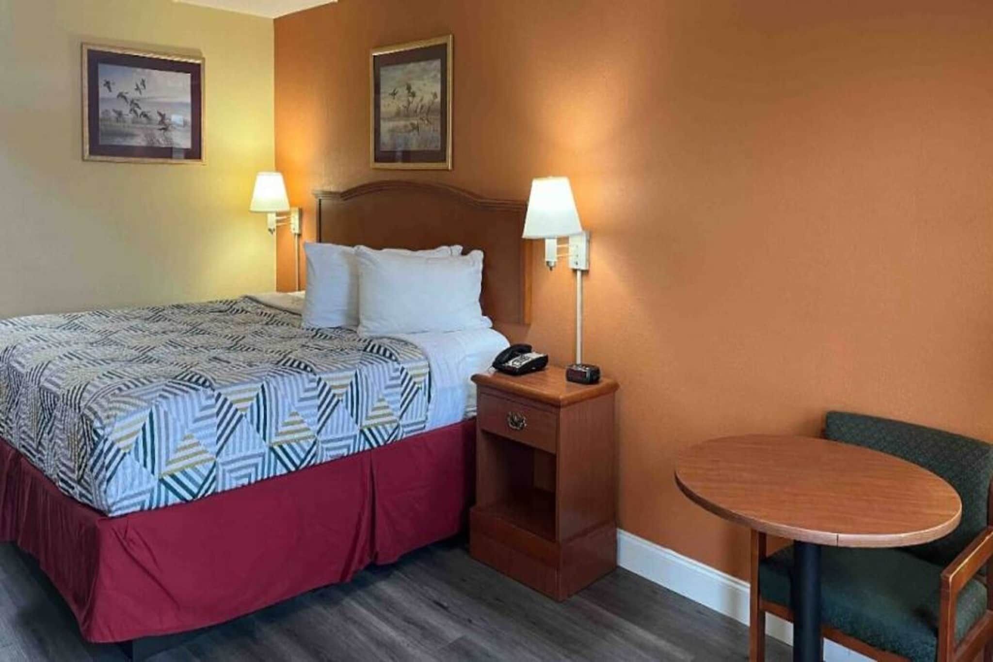 Une chambre d’hôtel comprenant un lit, des lampes de chevet, une table de chevet, une chaise et deux tableaux accrochés au mur.
