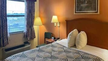 Ein Hotelzimmer mit einem großen Bett, zwei Nachttischlampen, einem Sessel, einem Schreibtisch mit Telefon und einem Vorhangfenster.