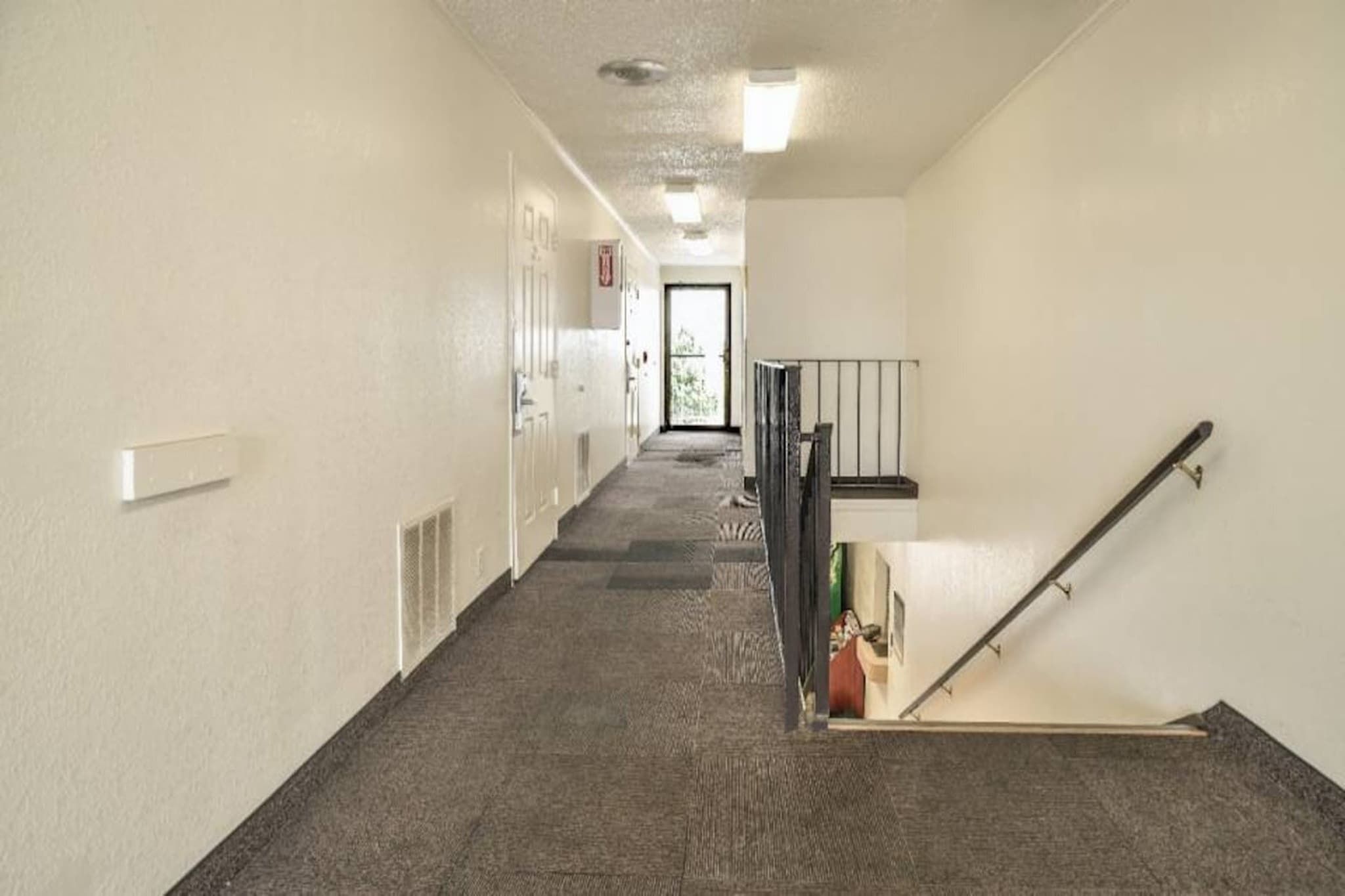 A hallway with carpeted floors, a staircase with a handrail, and a door at the end.