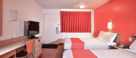 A hotel room with a desk, two beds, a television, and a red curtain.