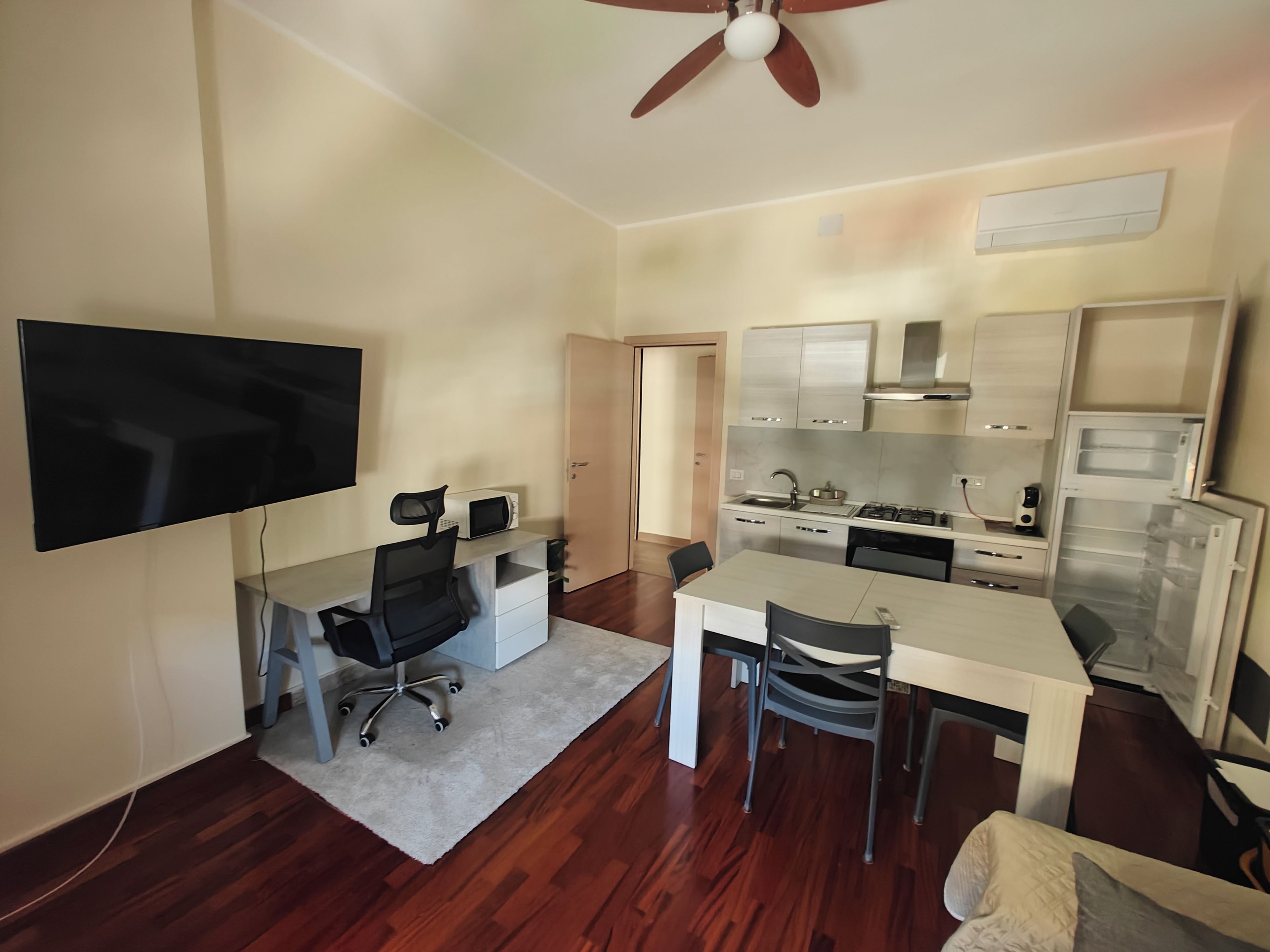 Un espacio habitable compacto con kitchenette, comedor y televisor montado en la pared.