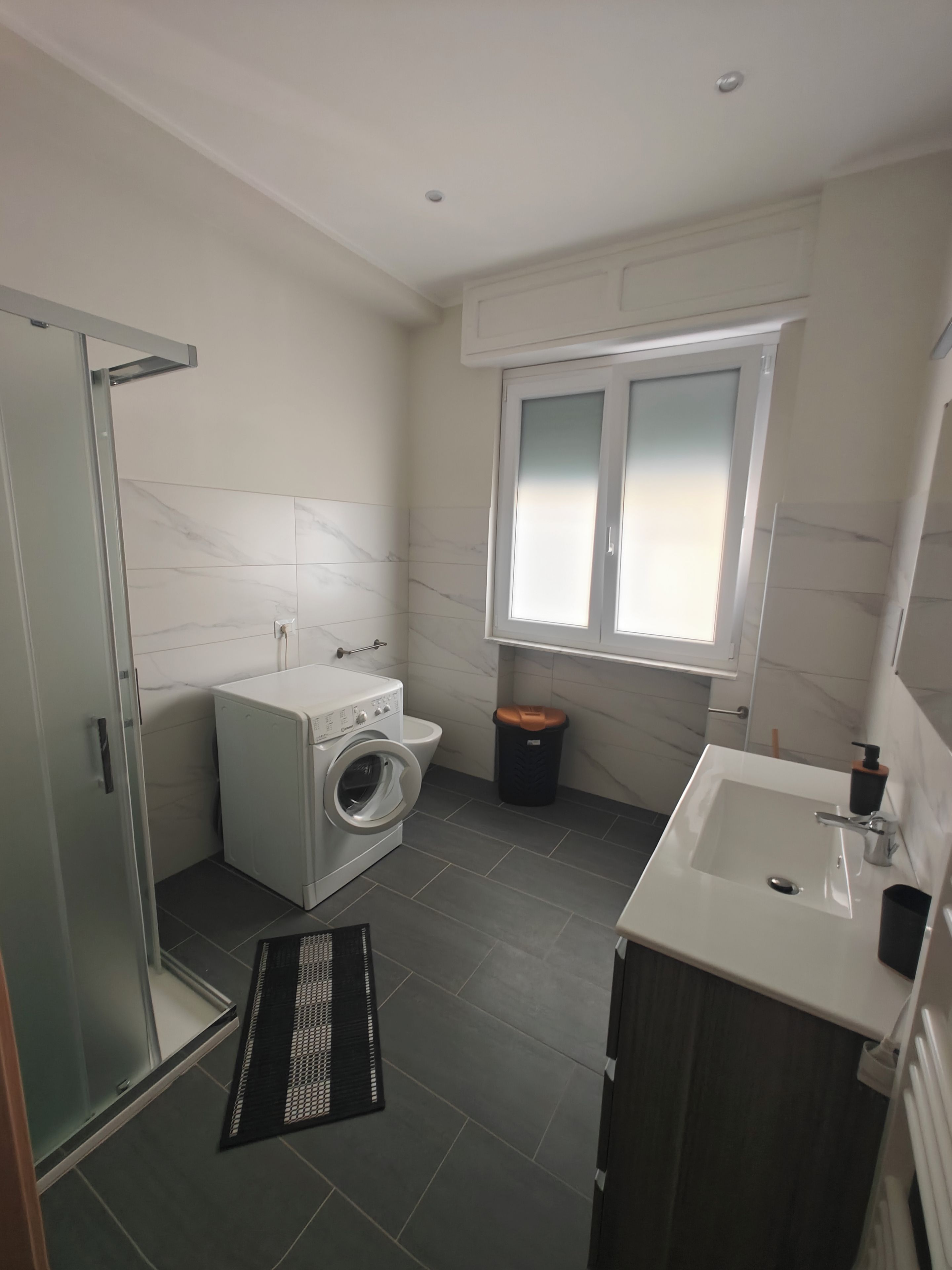 Une petite salle de bain dotée d’une douche à parois de verre, d’un lave-linge, de toilettes et d’un lavabo avec un miroir.